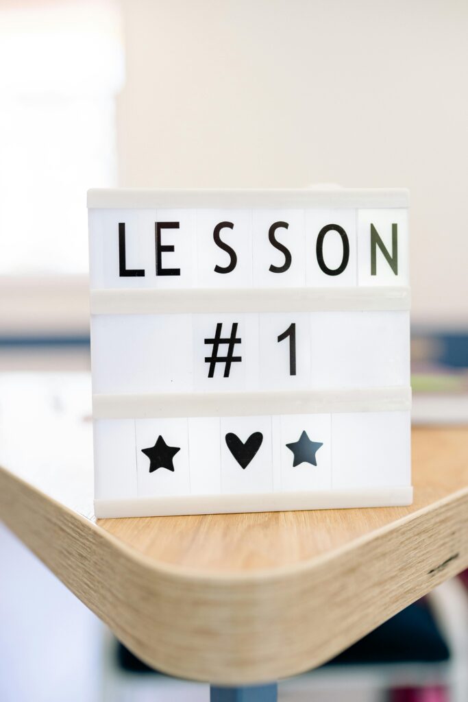 Letter board with the words "Lesson #1" on it, followed by a star image, then a heart, then another star. The letter board sits on a wooden table or desk.